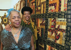 Rita-Cox-stands-in-front-of-quilts-with-sister-Linda-Powds-Gallery-Night-and-Day-Event-King-Drive-Commons